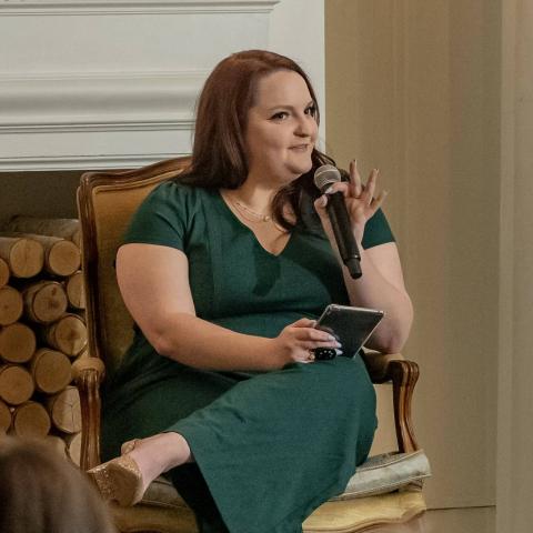 Author Thea Claire holds a microphone while speaking to an audience.