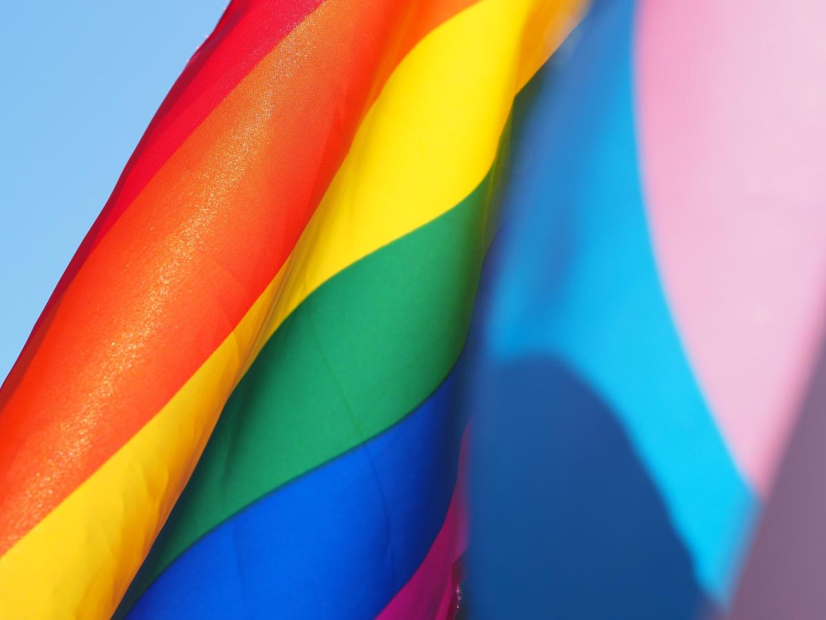 A Progress Pride flag ripples in the wind against a blue sky.