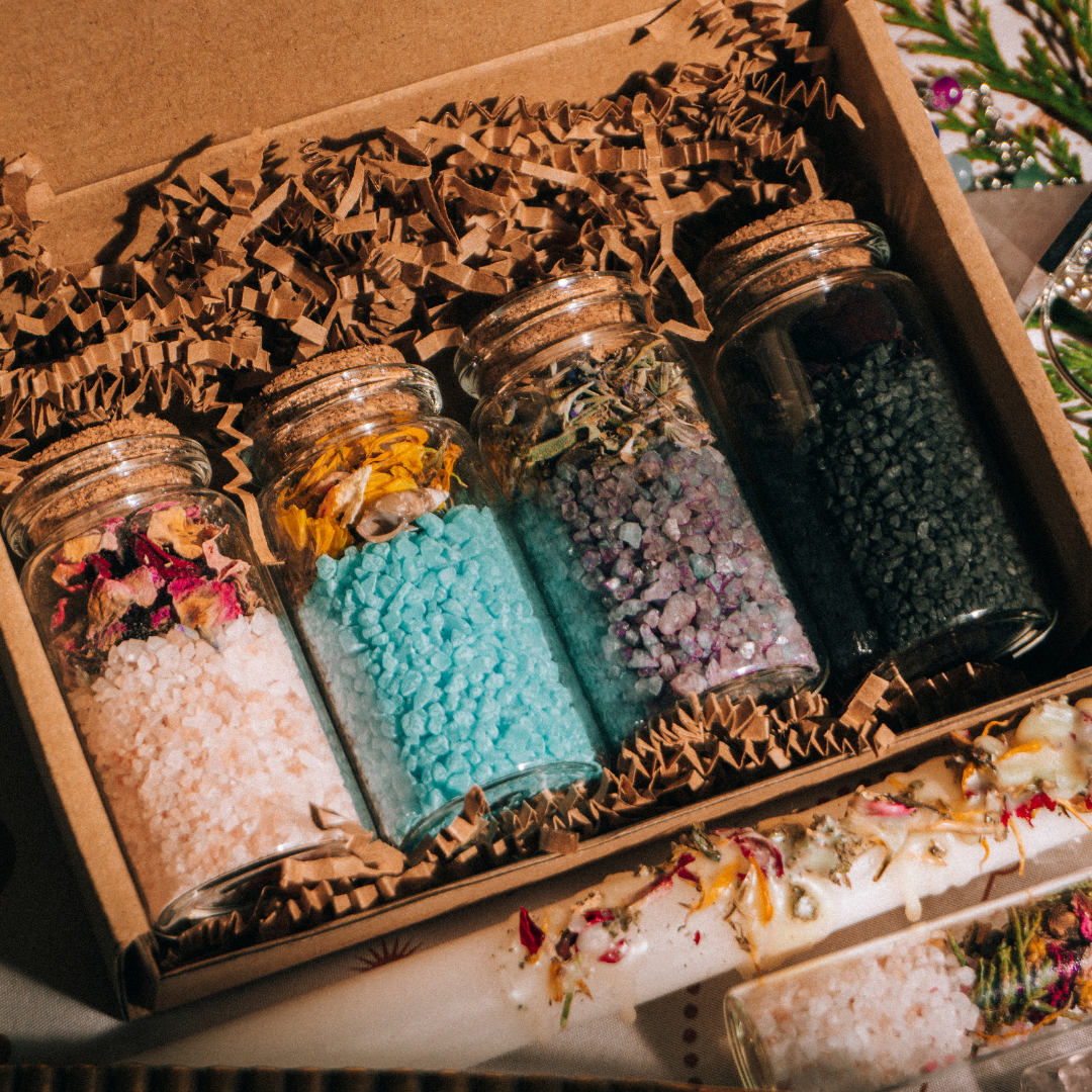 Differently colored bath salts with dried botanicals in corked jars.