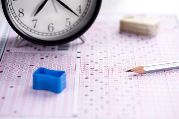 A clock, pencil, sharpener, and eraser rest atop a filled out standard testing form.