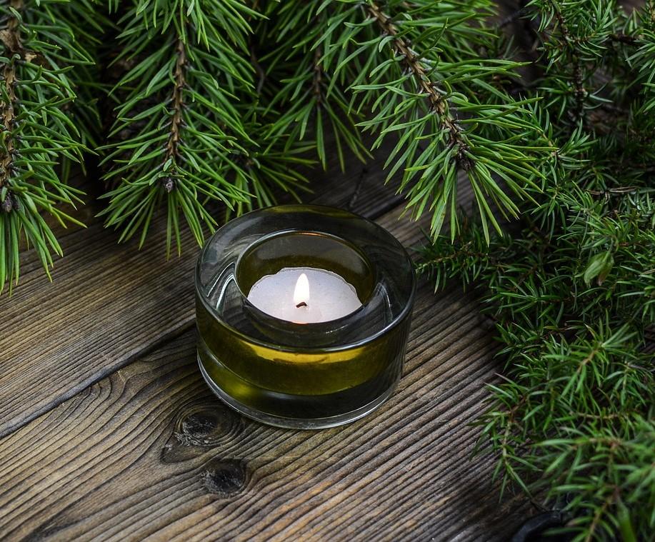candle in small tin surrounded by conifer leaves