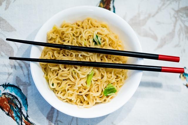 A bowl of ramen noodles sits on a white tablecloth with birds pictured on it. There are chopsticks laid across the top of the bowl.