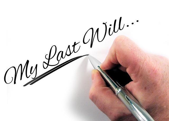 A hand is holding a silver pen over a white sheet of paper. It looks as if the hand has just written the words “My Last Will….” onto the paper.