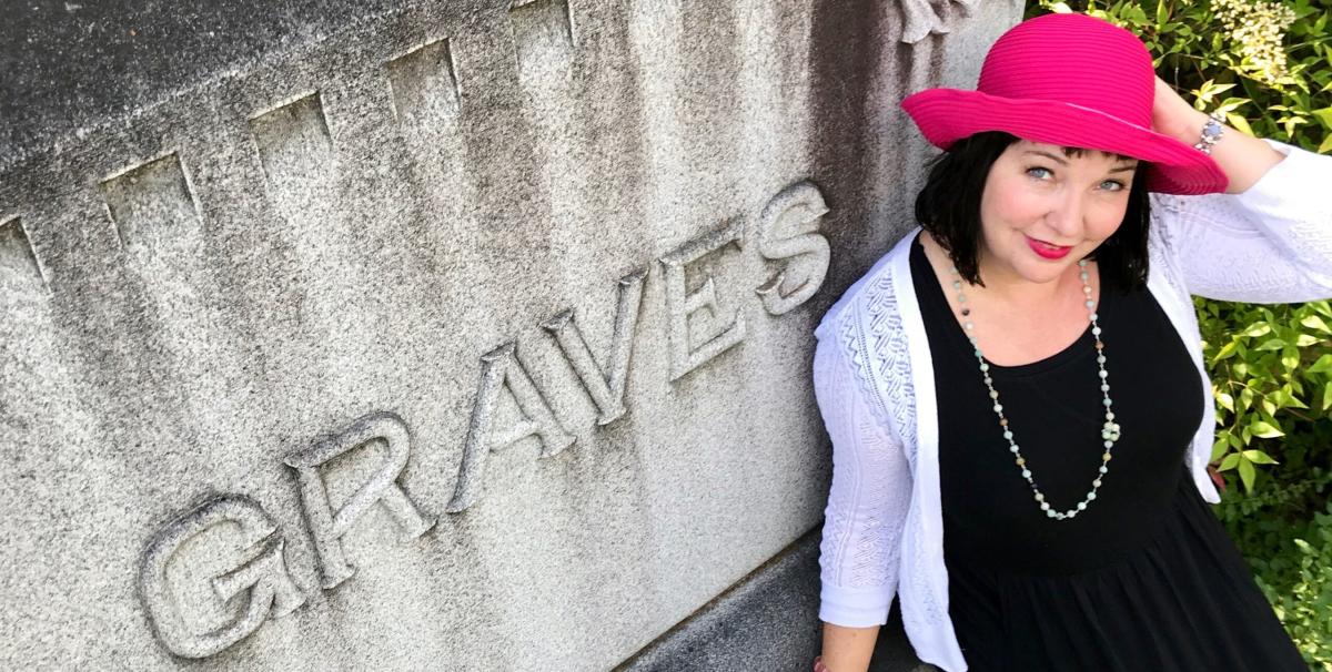 Author/Presenter Tui Snider standing next to a gravestone with the name of Graves