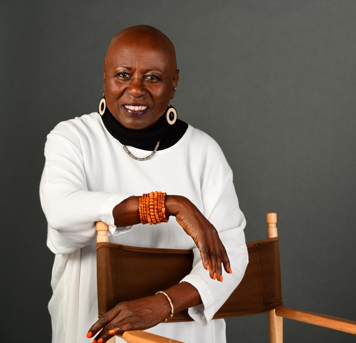 Linda Jones, a black woman, smiles at the camera. She wears a white shirt and orange bracelet.