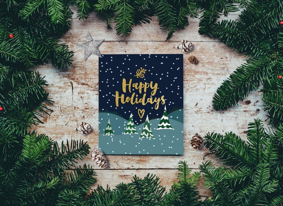 Holiday greeting card set in the center of surrounding fir. The card is set on top of wood, being decorated with stars and pine cones. Tarjeta de felicitación navideña situada en el centro del abeto circundante. La tarjeta está colocada sobre madera y decorada con estrellas y piñas.