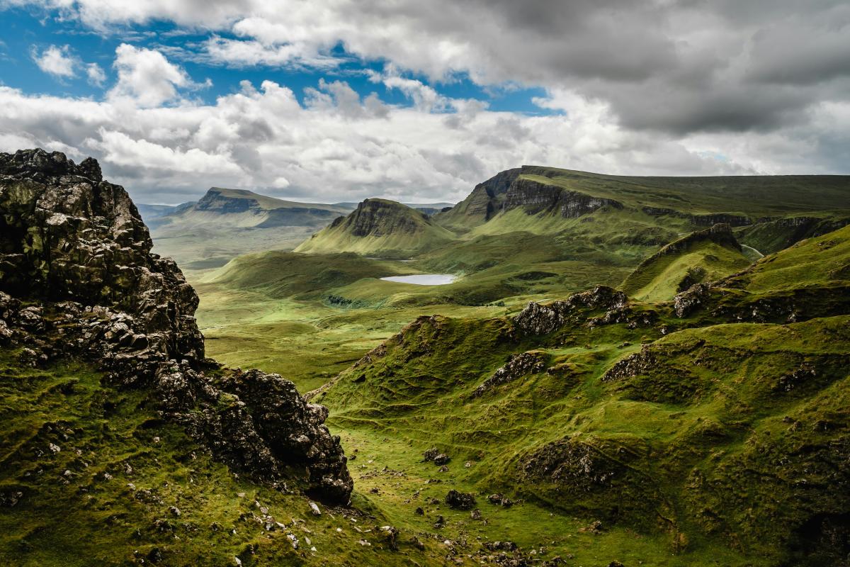 Isle of Sky, green grass among dark rock hills with a cloudy blue sky