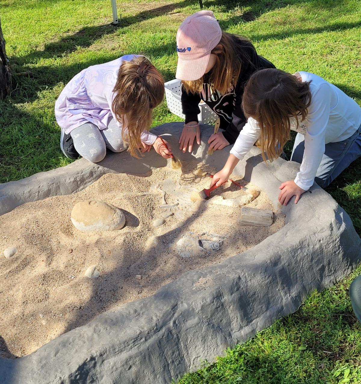 children examining a large dinosaur footprint