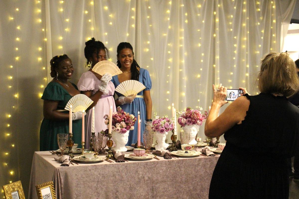 Three women pose coquettishly with fans for a photo with a fully decorated table. 