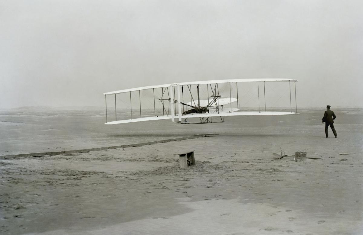 black and white photo of two men creating the first airplane on a beach
