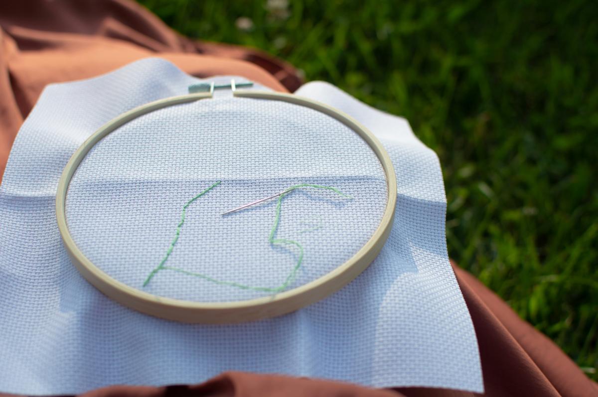 embroidery hoop with white fabric and a needle with green thread