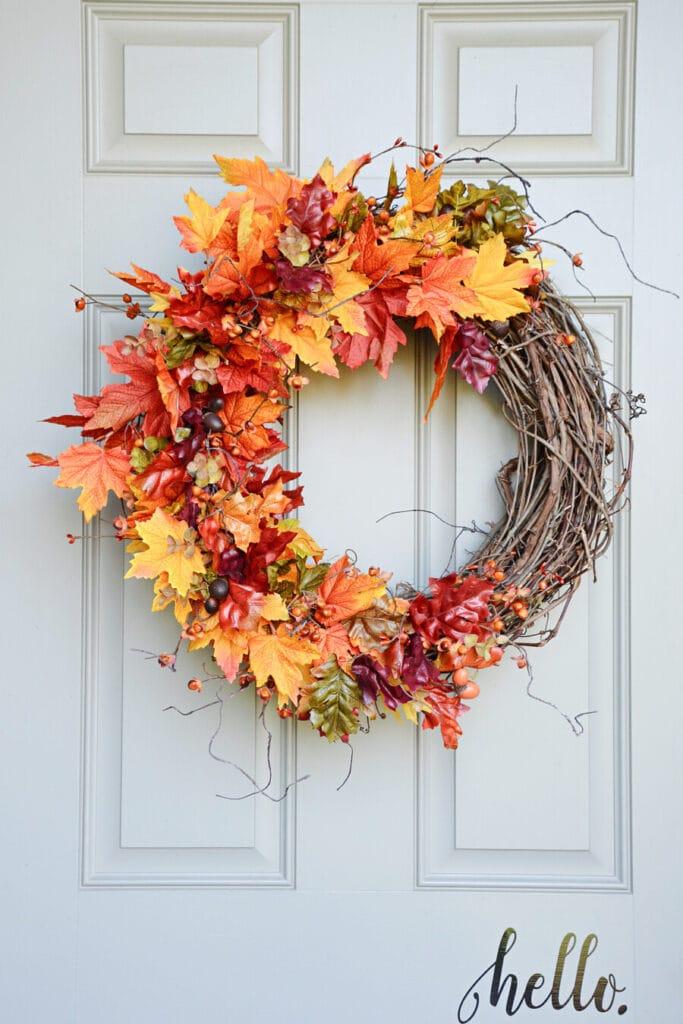 white front door with a grapevine wreath covered in yellow, orange, and red leaves