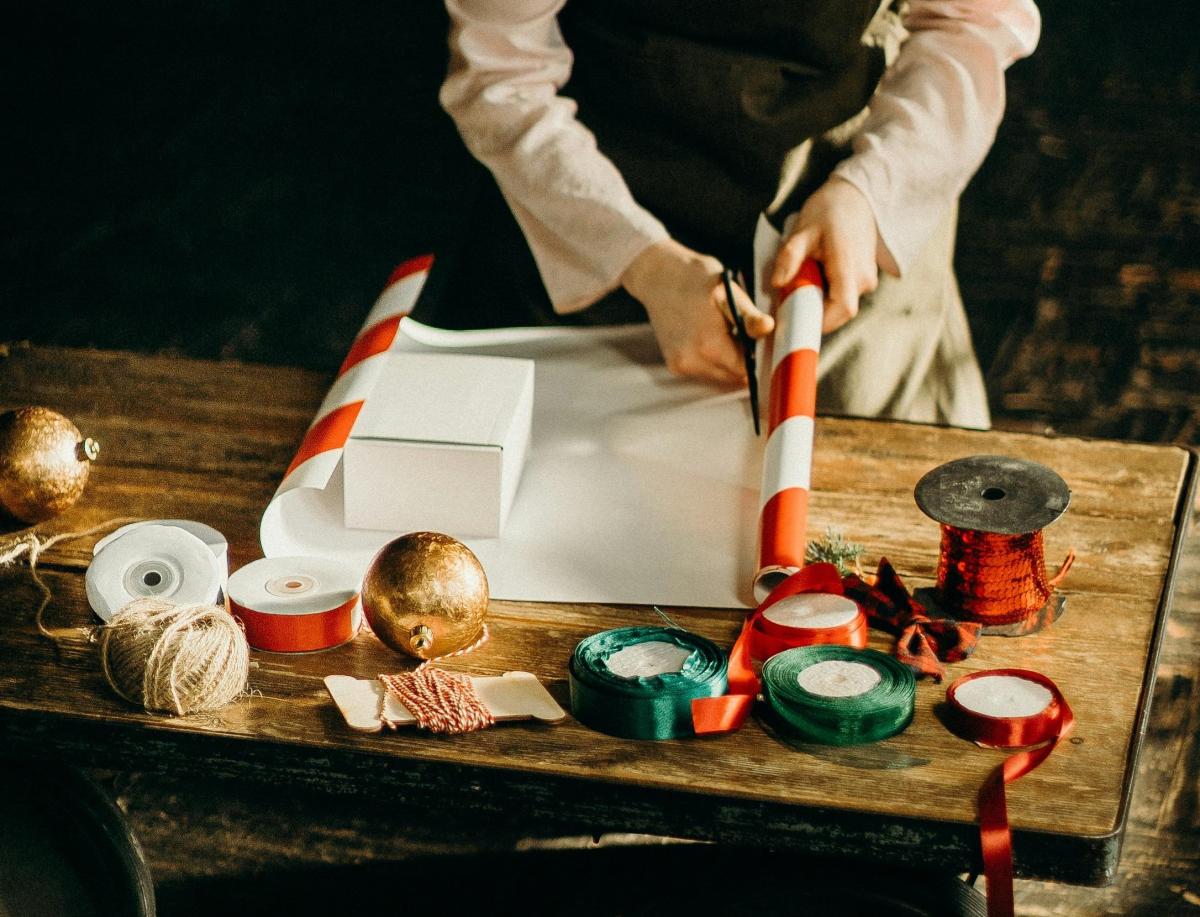 woman using scissors to cut gift wrapping paper. she is surrounded with ribbons, tape, and bows