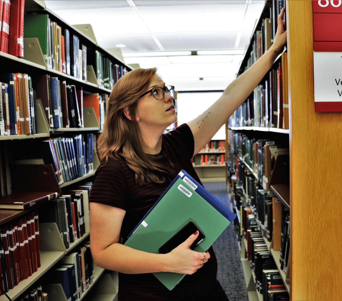 Person grabbing a book from the library shelf.
