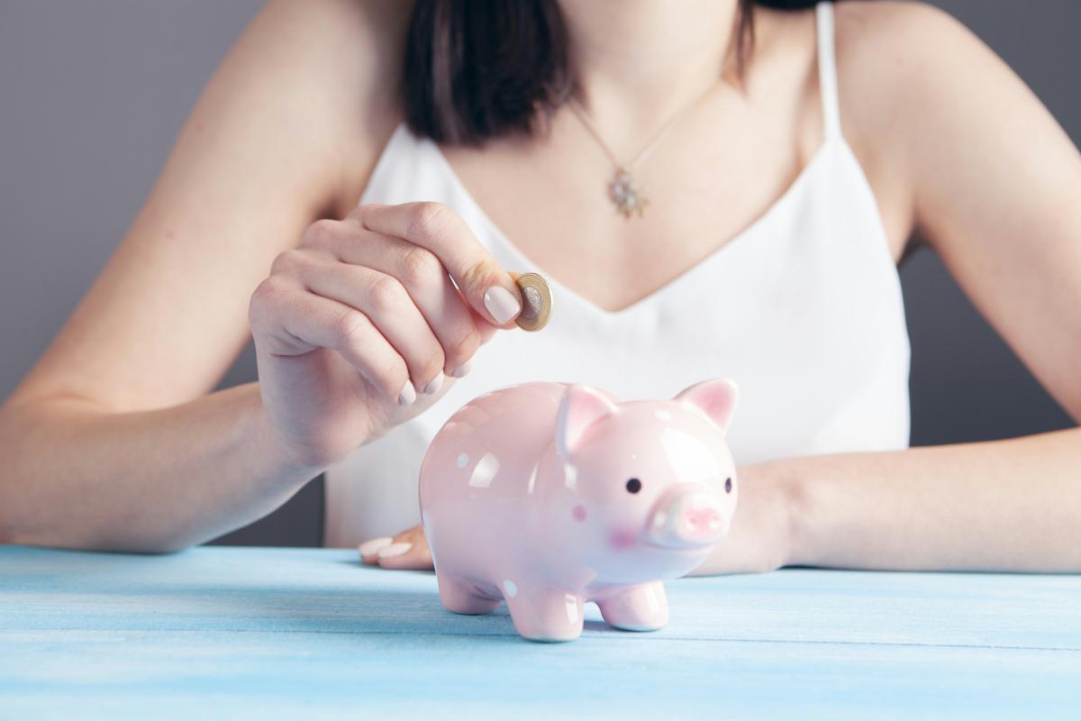 woman placing a coin into a pink piggy bank