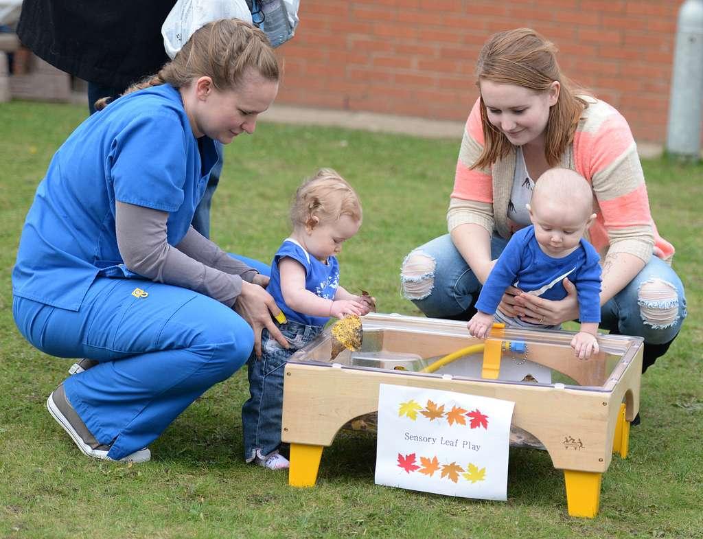 Two adults and two toddlers interact and play with a sensory bin.