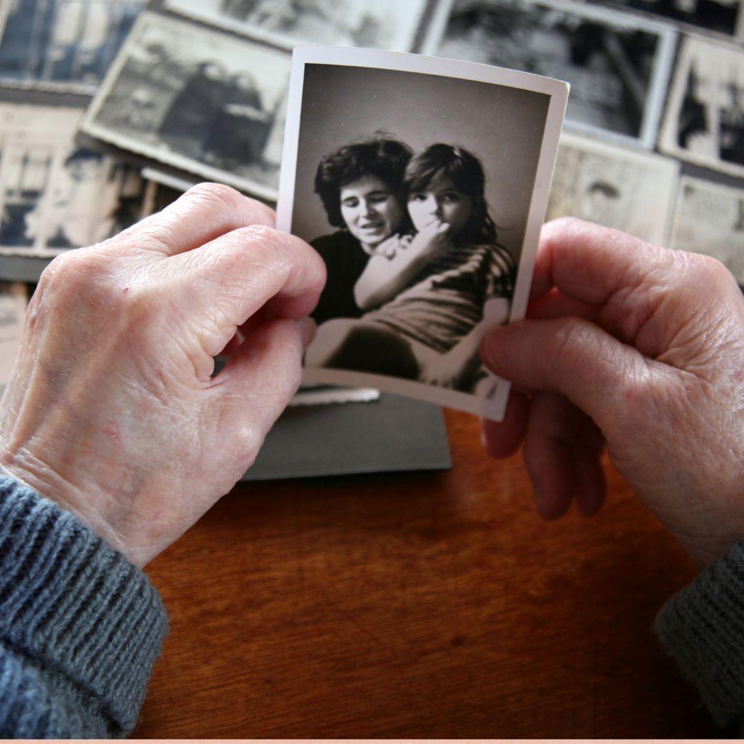 Old hands holding a picture of a mother and child over over a photo album
