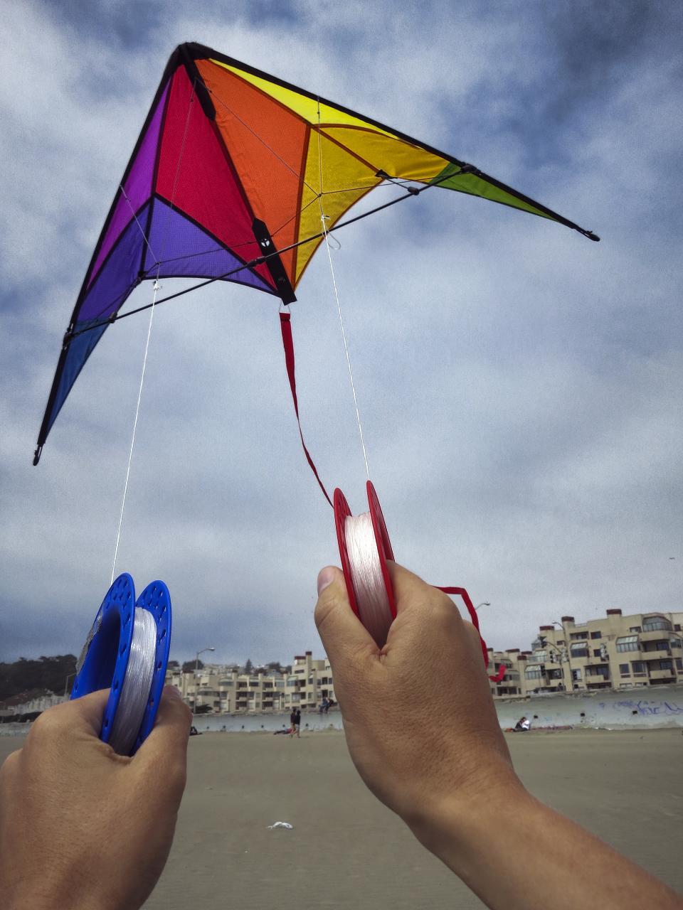 two hands holding the string of a brightly colored, flying kite